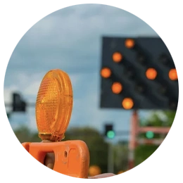 Orange construction warning light mounted on a barrier at a roadwork site with a signal board in the background.